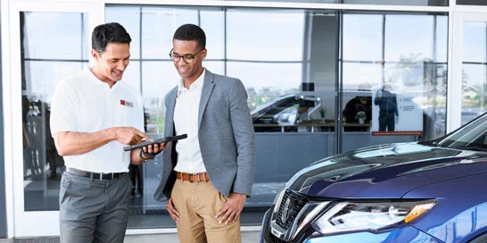 Nissan service consultant and a customer looking at a tablet in front of the dealership.