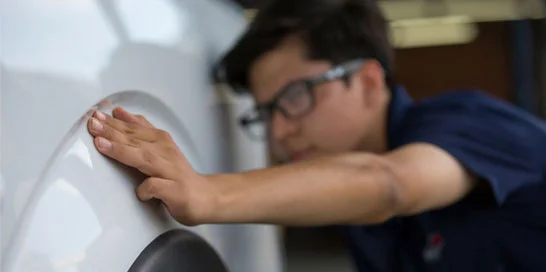 Technicien Nissan inspectant de près la carrosserie d’un véhicule.